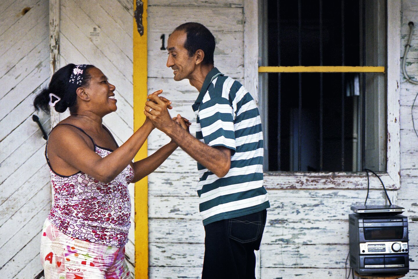 Gabriel 52 y.o. sanitation worker is dancing salsa with his second wife Mercedes, 47 y.o. on the doorstep of their old wooden home in San Francisco de Paula village of Havana where Hemingway used to live in his home Finca Vigia. They have been married for 10 years. Havana, Cuba. June 16, 2013 | © Rena Effendi 