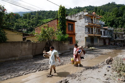 After the devastating flood of August 26, 2026, in northern Nepal, two local women wade through the water and mud. | © Keystone/EPA/Narendra Shrestha